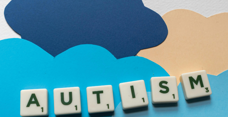 Scrabble tiles spell out the word Autism upon a background made of cut out paper clouds