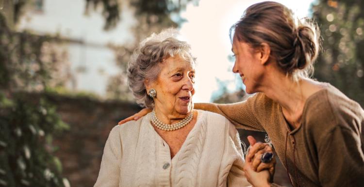 Two women are in a garden smiling as they speak to each other