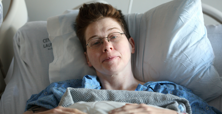 Woman lies on hospital bed looking into the lens of the camera