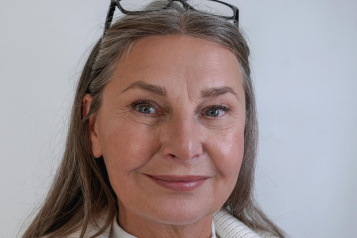 Woman over 55 with glasses on her head smiling to camera