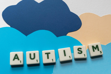 Scrabble tiles spell out the word Autism upon a background made of cut out paper clouds