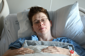 Woman lies on hospital bed looking into the lens of the camera