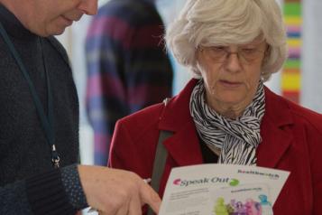 A woman looking at a Healthwatch leaflet while a man points